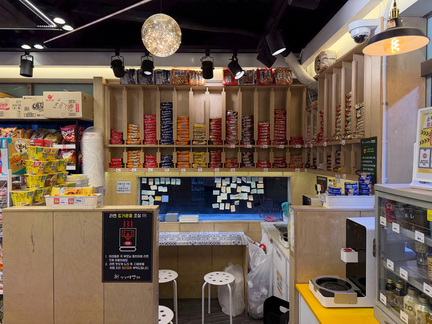 Auto-generated description: A cozy Korean snack shop features shelves filled with various packaged snacks and a small counter area with stools.